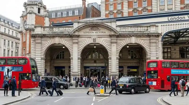 The stone front of London Victoria station with red buses and passengers outside